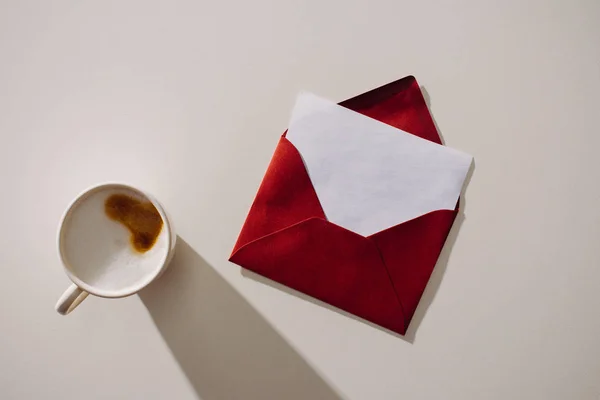 Vue du dessus de l'enveloppe rouge avec du papier blanc et une tasse de café — Photo de stock