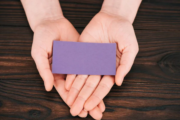 Ritagliato colpo di donna in possesso di carta viola vuota su tavolo di legno — Foto stock