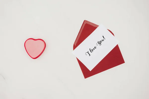 Top view of red envelope with i love you lettering on paper and heart shaped box isolated on white — Stock Photo