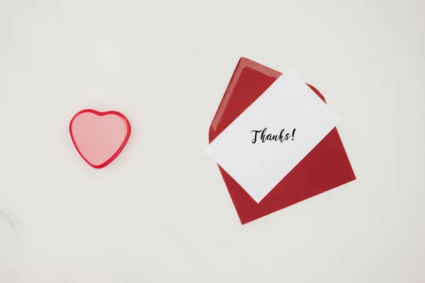 Top view of red envelope with THANKS lettering on paper and heart shaped box isolated on white — Stock Photo