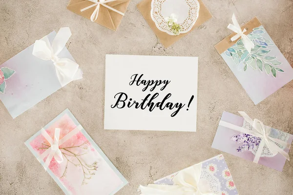 Vista superior de papel con letras de feliz cumpleaños rodeado de tarjetas de felicitación en la superficie de hormigón - foto de stock
