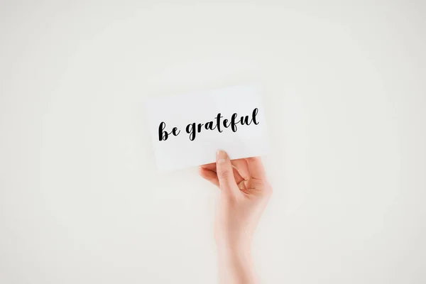 Cropped shot of woman holding paper with be grateful lettering isolated on white — Stock Photo