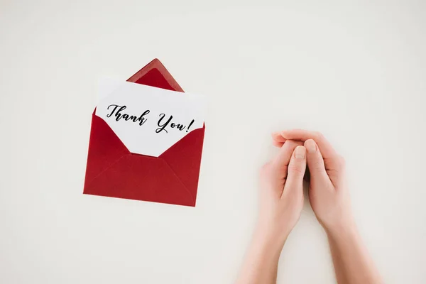 Colpo ritagliato di donna che si tiene per mano vicino alla busta rossa aperta con scritte di ringraziamento su carta isolata su bianco — Foto stock