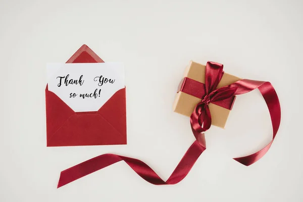 Top view of red envelope with thank you so much lettering on paper and gift box isolated on white — Stock Photo