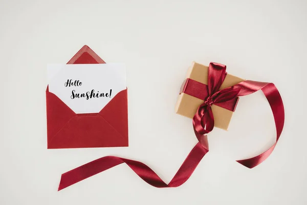 Vue du dessus de l'enveloppe rouge avec lettrage bonjour soleil sur papier et boîte cadeau isolé sur blanc — Photo de stock