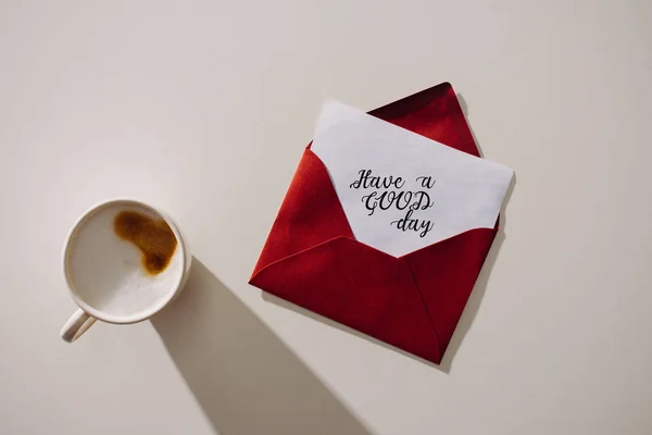 Draufsicht auf roten Umschlag mit einem guten Tag Schriftzug auf Papier und Tasse Kaffee — Stockfoto