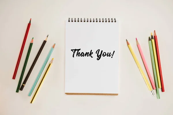 Top view of notepad with thank you lettering and colorful pencils isolated on white — Stock Photo