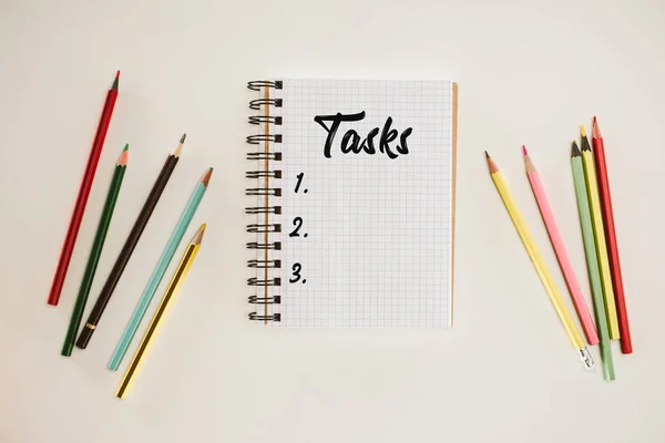 Vue du haut du bloc-notes avec des tâches vierges liste lettrage et crayons colorés isolés sur blanc — Photo de stock