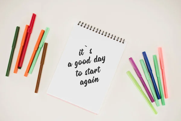 Top view of notepad with its a good day to start again lettering and colorful markers isolated on white — Stock Photo