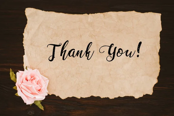 Vue du dessus du papier vieilli avec lettrage de remerciement et fleur rose sur table en bois — Photo de stock