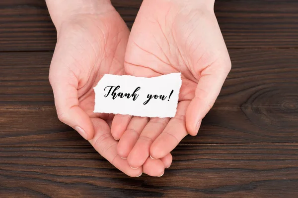 Abgeschnittene Aufnahme einer Frau, die Papier mit Dankeschön-Schriftzug über Holztisch hält — Stockfoto