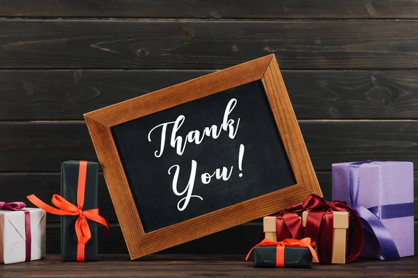 Thank you lettering on chalkboard in frame with various gift boxes against wooden wall — Stock Photo