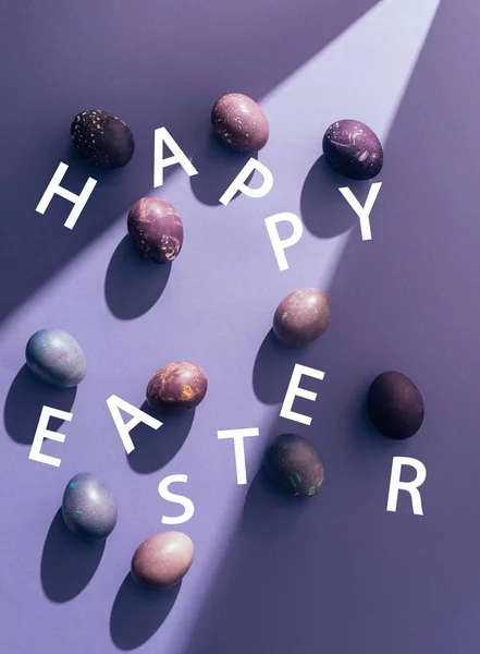 Великодні фіолетові яйця з щасливим великоднім листям на фіолетовому фоні з сонячним промінням — стокове фото