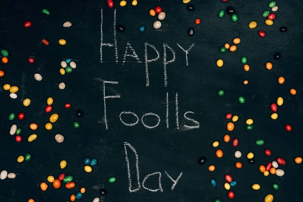 Flat lay with sweets and happy foolls day lettering on black tabletop — Stock Photo