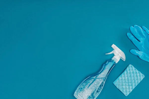 Vue du dessus du flacon pulvérisateur et du gant en caoutchouc avec éponge de lavage isolé sur bleu — Photo de stock