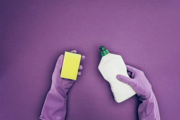 Imagem cortada de mulher segurando esponja de lavagem e fluido de limpeza isolado em violeta — Fotografia de Stock