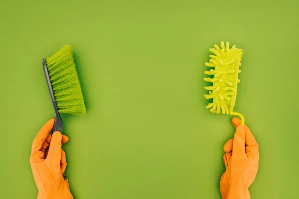 Imagem cortada de mulher segurando duas escovas de limpeza diferentes em mãos isoladas em verde — Fotografia de Stock