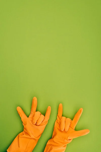 Imagen recortada de la mujer que muestra signos de roca en guantes protectores de goma aislados en verde - foto de stock