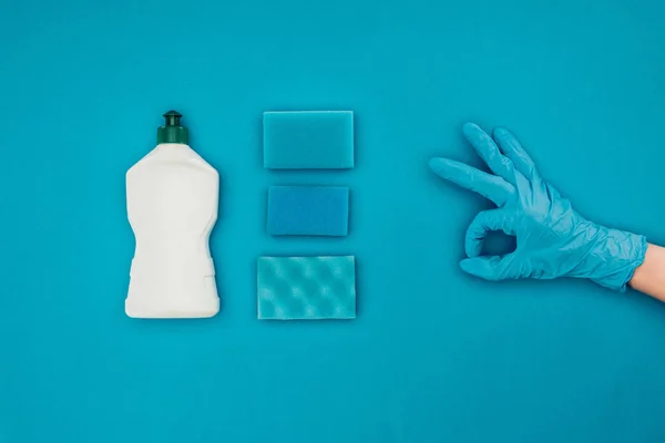 Imagen recortada de la mujer que muestra signo ok en guante protector de goma aislado en azul - foto de stock