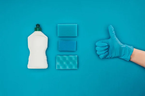 Cropped image of woman showing thumb up in rubber protective glove isolated on blue — Stock Photo
