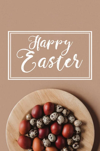Vue du dessus des oeufs de Pâques sur une assiette en bois avec inscription Joyeuse Pâques — Photo de stock