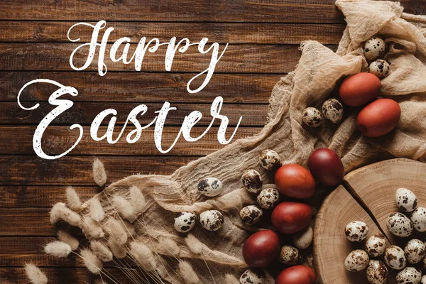 Flat lay with easter eggs and ears on cross section of tree trunk and gauze on wood background with Happy Easter inscription — Stock Photo