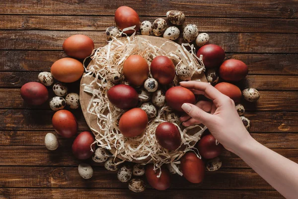 Vista recortada de la mano con huevos de Pascua en la sección transversal del tronco del árbol sobre fondo de madera - foto de stock