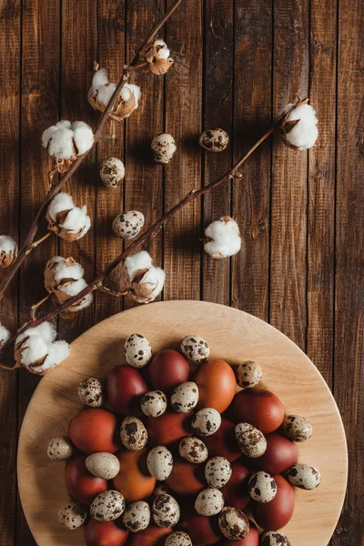 Flat lay with chicken and quail eggs on plate on wood background with cotton flowers — Stock Photo