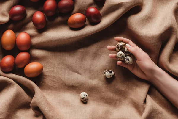 Cropped view of hand with quail eggs on tablecloth with easter eggs — Stock Photo