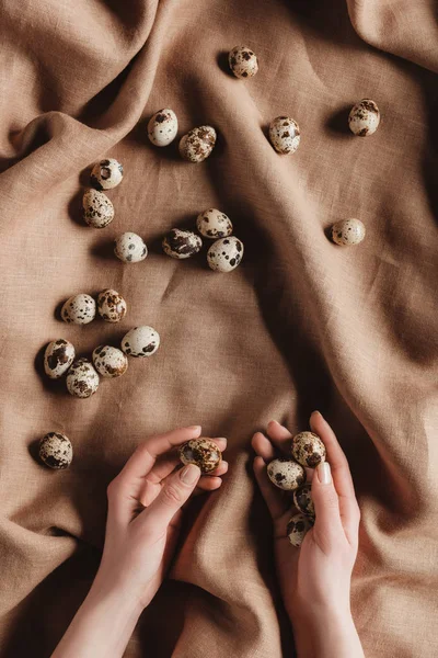 Cropped view of person holding quail eggs in hands on tablecloth — Stock Photo