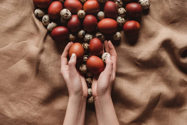 Cropped view of hands with easter painted eggs and quail eggs on tablecloth — Stock Photo