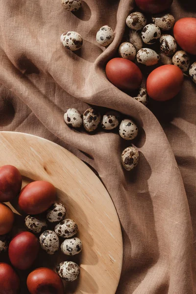 Flat lay with easter painted eggs and quail eggs on wooden plate — Stock Photo