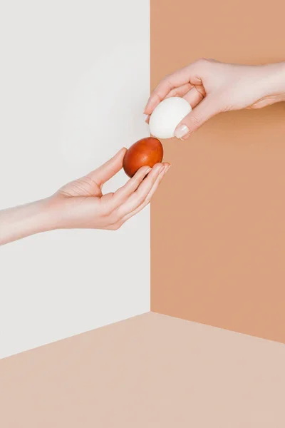 Cropped view of people with easter eggs on beige and white minimalistic background — Stock Photo