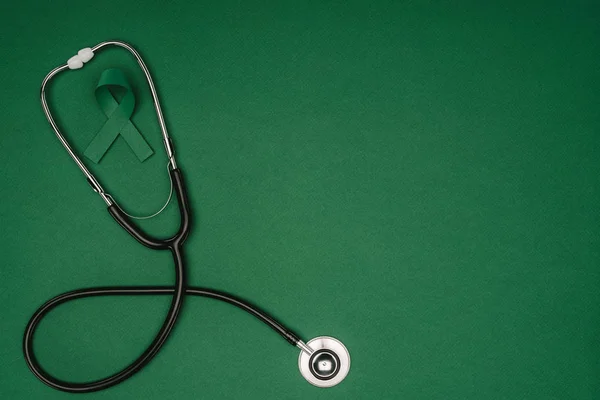 Vista superior de la cinta verde de la conciencia para la escoliosis, símbolo de la salud mental y estetoscopio aislados en la superficie verde - foto de stock