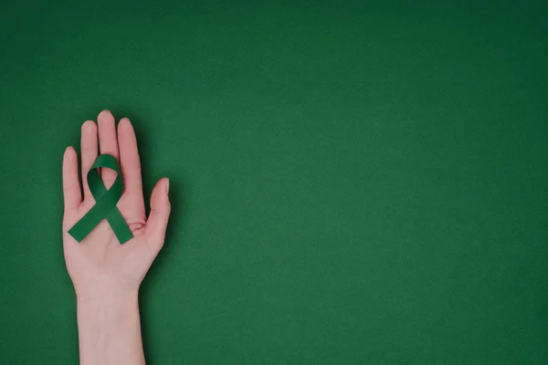 Tiro recortado da mão feminina com fita de consciência verde para fita de consciência verde para escoliose, símbolo de saúde mental isolado na superfície verde — Fotografia de Stock