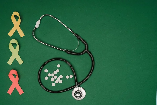 Posa piatta con pillole organizzate, nastri colorati e stetoscopio isolato su tavolo verde, concetto giornata mondiale della salute — Foto stock