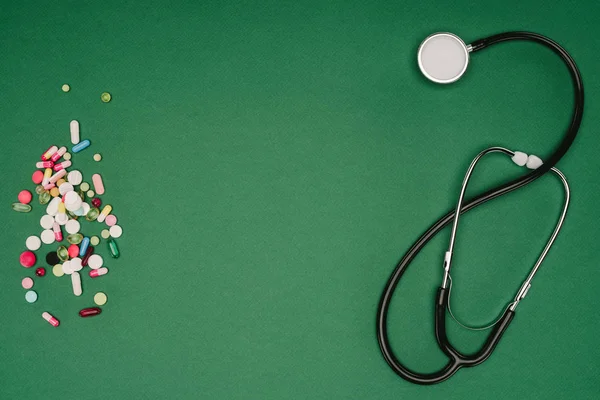 Плоский шар з організованими таблетками і стетоскопом ізольований на зеленому столі, концепція Всесвітнього дня здоров'я — стокове фото