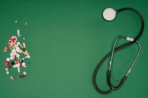 Plano yacía con píldoras arregladas y estetoscopio aislado en la mesa verde, concepto del día de la salud mundial - foto de stock