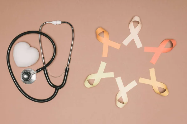 Vista dall'alto di cuore organizzato, stetoscopio e nastri colorati isolati sulla superficie beige, concetto giornata mondiale della salute — Foto stock