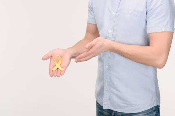 Tiro recortado del hombre que muestra la cinta amarilla de la conciencia del cáncer de la niñez aislada en blanco - foto de stock