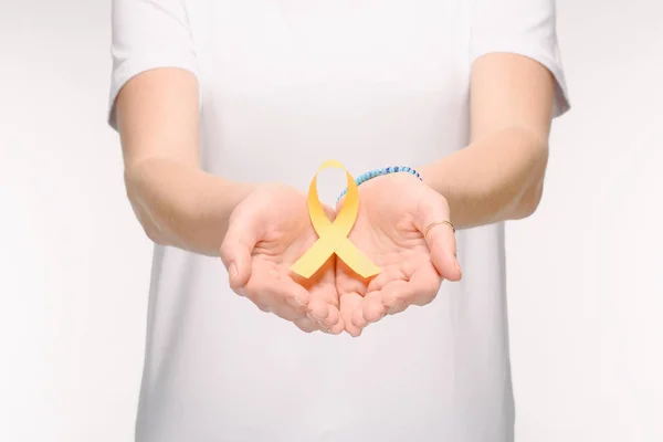 Cropped shot of woman holding Childhood Cancer Awareness ribbon in hands isolated on white — Stock Photo
