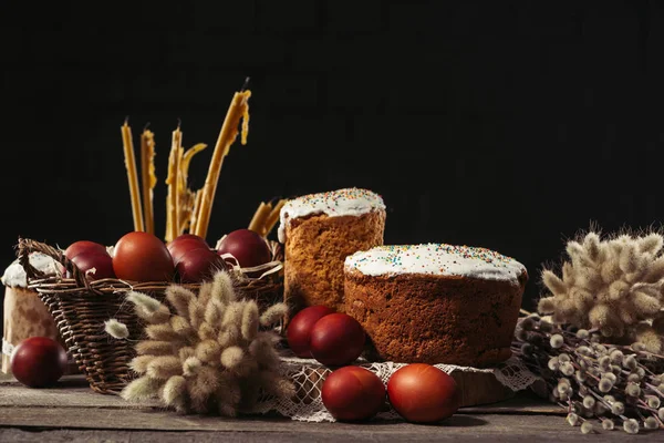 Close-up view of delicious homemade easter cakes, painted chicken eggs, willow twigs and candles on black — Stock Photo