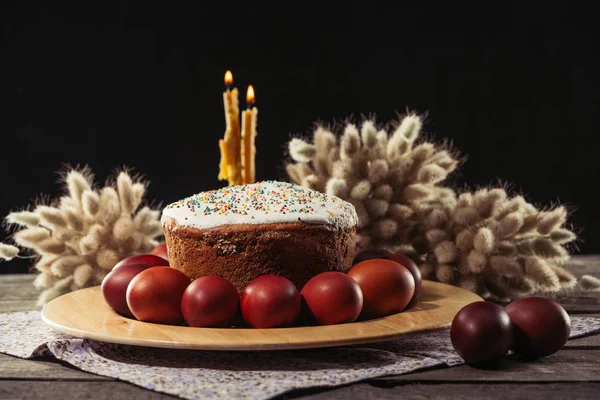 Painted chicken eggs, easter cake and burning candles on wooden table — Stock Photo