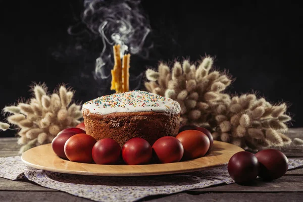 Painted chicken eggs, homemade easter cake and candles with smoke on black — Stock Photo