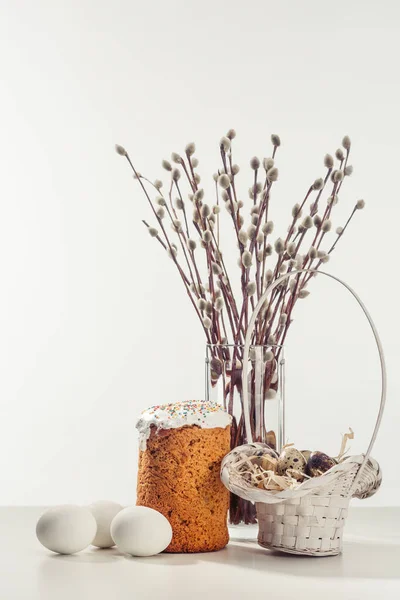 Oeufs de caille dans le panier, oeufs de poulet, gâteau de Pâques et brindilles de saule en vase sur gris — Photo de stock