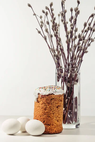 Nahaufnahme von Hühnereiern, hausgemachtem Osterkuchen und Weidenzweigen in Vase auf grau — Stockfoto