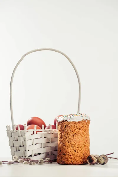 Декоративная корзина с покрашенными куриными яйцами, пасхальным тортом, перепелиными яйцами и кексами на сером — стоковое фото