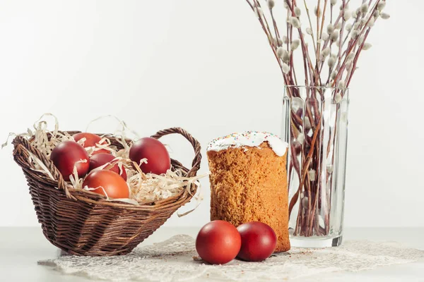 Painted chicken eggs in basket, easter cake and catkins in vase on grey — Stock Photo