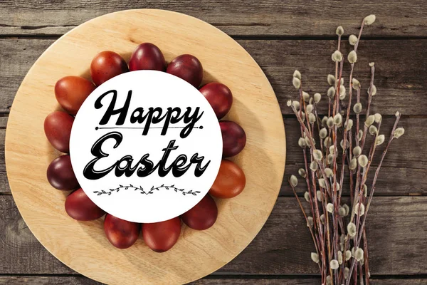 Top view of painted easter eggs with happy easter inscription and willow twigs on wooden table — Stock Photo