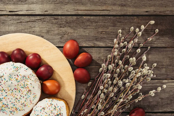 Top view of painted chicken eggs, easter cakes and catkins on wooden surface — Stock Photo